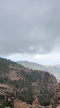 İspanya, Gran Canaria 'daki dağların ve volkanik kayalık tepelerin çarpıcı manzarası. Gökyüzü bulutlu ve puslu. Dağlar arasındaki vadide birçok ev, bina ve yol olan bir kasaba var..