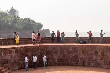 Candolim, Goa, Hindistan - Ocak 2023: Sinquerim 'deki antik Portekiz döneminden kalma kalenin duvarlarında deniz manzarasının keyfini çıkaran büyük bir grup Hintli turist.