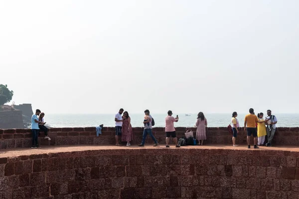 stock image Candolim, Goa, India - January 2023: Large group of Indian tourists enjoying the view of the sea on the walls of the ancient Portuguese era fort in Sinquerim.