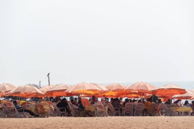 Calangute, Goa, Hindistan - Ocak 2023: Turuncu şemsiyeler ve hasır sandalyeler Calangute sahilindeki bir lokanta barakasında.