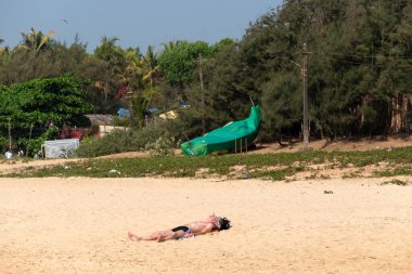 Calangute, Goa, Hindistan - Ocak 2023: Erkek bir turist güneşleniyor ve boş bir plajda uzanarak güneşleniyor.