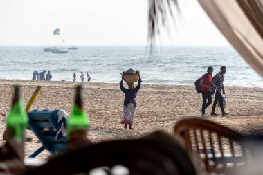 Calangute, Goa, Hindistan - Ocak 2023: Goa 'da bir plajda kafasında meyve sepeti taşıyan Hintli bir kadın satıcı.