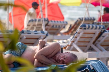 Calangute, Goa, Hindistan - Ocak 2023: Goa 'da bir sahil barakasında güverte sandalyesinde uyuyan beyaz bir erkek turist.