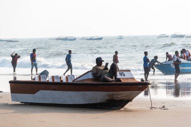 Calangute, Goa, Hindistan - Ocak 2023: Goa 'da kalabalık bir sahilde teknesinde yatan Hintli bir balıkçı.