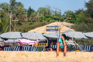 Calangute, Goa, Hindistan - Ocak 2023: Beyaz bir kadın turist bir barakanın önünde tek başına oturuyor.