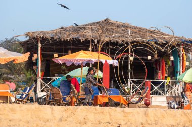 Calangute, Goa, Hindistan - Ocak 2023: Calangute 'da bir sahil kulübesinin önünde süpürgeyle yerleri temizleyen bir kadın işçi.