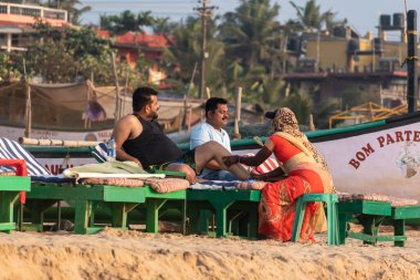 Calangute, Goa, Hindistan - Ocak 2023: İki Hintli erkek turist sahil barakasında bir kadından masaj yaptırıyor.