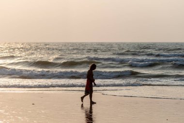 Calangute, Goa, Hindistan - Ocak 2023: Boş bir sahilde tek başına yürüyen Kafkas turistlerin arka aydınlatma silueti.