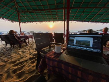 Calangute, Goa, Hindistan - Ocak 2023: Calangute sahilindeki bir kafede bir fincan kahve ve bir dizüstü bilgisayar.