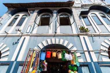 Margao, Goa, Hindistan - Ocak 2023: Madgaon 'da eski bir Portekiz döneminden kalma bir binanın kemerlerinin altında renkli kova satan bir dükkanın düşük açılı çekimi.