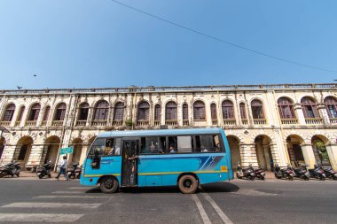 Margao, Goa, Hindistan - Ocak 2023: Madgaon kentindeki antik belediye meclisi binasının önünden geçen mavi bir toplu taşıma otobüsü.