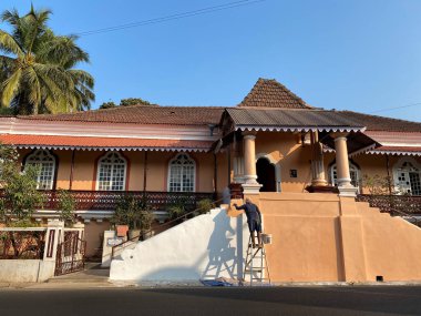 Margao, Hindistan - 21 Ocak 2023: Güney Goa 'da geleneksel mimarisi olan eski bir evin duvarlarını boyayan bir adam.