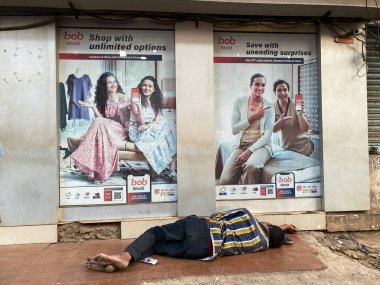 Margao, Hindistan - 21 Ocak 2023: Reklamların önünde uyuyan fakir bir Hintli sınırsız alışveriş yapıyor.