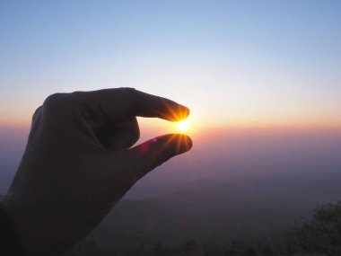 Silhouette of Hand picking sun at sunrise sky on the top of mountain background.