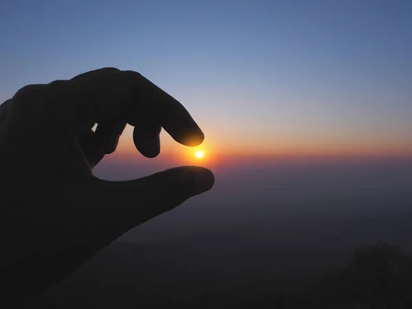 Silhouette of Hand picking sun at sunrise sky on the top of mountain background.