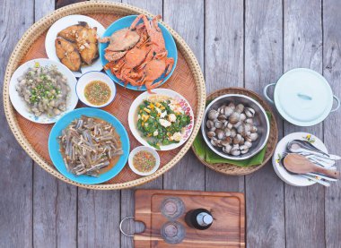 Tahta masanın üzerinde bambu tepside servis edilen Tayland deniz ürünleri seti. Kabuklu deniz ürünleri, kızarmış balık ve baharatlı yengeç..