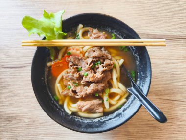 Domuz etli Udon çorbası, sebzeler ve ahşap masada siyah kâse çorbası, üst manzara. Tonkotsu ramenini kapat. Japon yemeği..