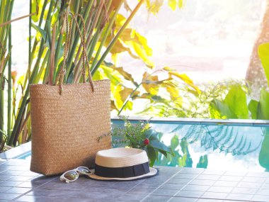 Doğal tatil köyünde yüzme havuzunun yanında şapka ve güneş gözlüğüyle örülmüş çantayı kapat. Tatil konseptinde rahatlama.