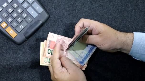 手里拿着计算器在桌上数着巴西钞票的人的手 — 图库视频影像