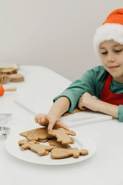 サンタの帽子のかわいい男の子は 鹿の形をした焼きたてのクリスマス休暇クッキーを手に入れます クリスマス休暇 — ストック写真