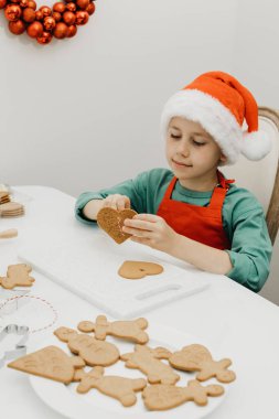 Noel Baba şapkalı şirin bir çocuk, mutfakta Noel süsüsüyle süslenmiş kalp şeklinde zencefilli kurabiye deliğine bir ip geriyor. Noel tatili konsepti