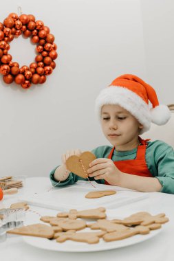 Noel Baba şapkalı şirin bir çocuk, mutfakta Noel süsüsüyle süslenmiş kalp şeklinde zencefilli kurabiye deliğine bir ip geriyor. Noel tatili konsepti