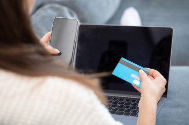 Online payment, a woman holds a smartphone and uses a credit card for online purchases. The concept of online shopping, online payment using a laptop computer clipart