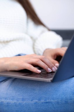 Dizüstü bilgisayarda klavyeye basan kadın ellerinin yakın çekimi. Bir kadın evde kot pantolonla kanepede otururken dizüstü bilgisayar kullanıyor..
