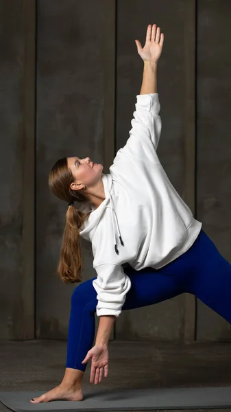 The athlete stands in the triangle pose. Pilates and yoga training. The woman makes a tilt to the side while standing.