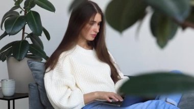 Çekici, genç, esmer bir kadın evinde dizüstü bilgisayarla çalışıyor. Uzaktan öğrenme, bilgi alma, bir dizüstü bilgisayar kullanarak.