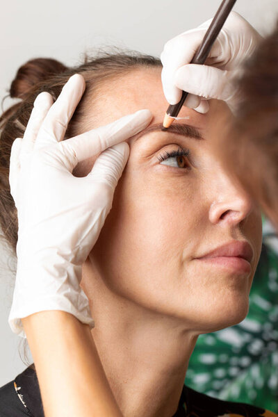 A permanent makeup artist draws eyebrows to a girl. The procedure for coloring and shaping eyebrows. Drawing the contour of the eyebrows before the microblading procedure.