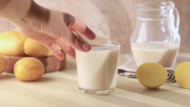 手はジャガイモミルクのガラスに達する 乳糖を含まない牛乳は ビーガン向けの飲み物です 牛乳代用品 ベジタリアン用牛乳 — ストック動画