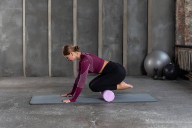 A young woman in sportswear performs a myofascial massage of the lower leg muscles with a roller on a gym mat. Muscle recovery, stress relief for muscle pain. mfr. clipart