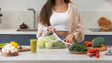 Bir kadın mutfakta dikilirken pamuk torbadan taze sebzeleri alır. Çevresel dostluk kavramı, sıfır batı. Vejetaryenlik, sağlıklı beslenme..