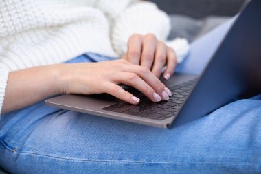 Dizüstü bilgisayarda klavyeye basan kadın ellerinin yakın çekimi. Bir kadın evde kot pantolonla kanepede otururken dizüstü bilgisayar kullanıyor..