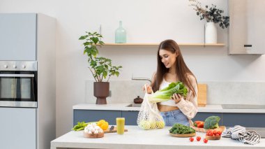 Çekici bir kadın gülümser ve mutfaktaki ağdan taze yiyecek çıkarır. Sıfır atık kavramı, sağlıklı bir yaşam tarzı ve sağlıklı bir diyet..