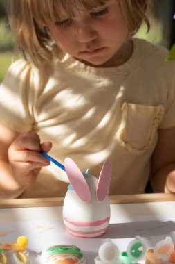 Küçük tatlı bir kız, bir Paskalya yumurtasını tavşan şeklinde süslüyor. Çocuklu Paskalya el sanatları fikirleri. Mutlu Paskalyalar. Yaratıcılık ve hobiler.