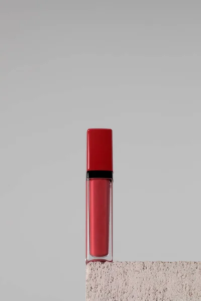 Moisturizing red lip balm on a stone pedestal on grey background. Makeup concept, lip care.