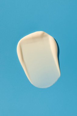 Örnekler. Beyaz bir kozmetik ürünün dokusu, mavi arka planda krem. Cilt bakımı kozmetik ürünleri. Cilt bakımı.