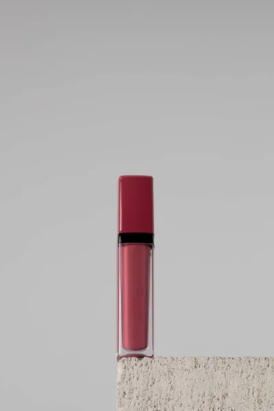 Moisturizing dusty pink lip balm on a stone pedestal on grey background. Makeup concept, lip care.