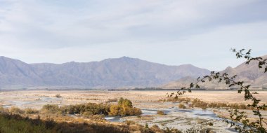 Dağlarla çevrili bir nehri olan bir vadi manzarası. Yeni Zelanda 'nın güney adasında bir doğa sahnesi. Vahşi doğa güzelliği kavramı.