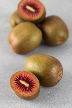 Kırmızı kivi bütünü ve gri masada ikiye bölünmüş. Tropik meyve konsepti, kivi çeşitliliği.