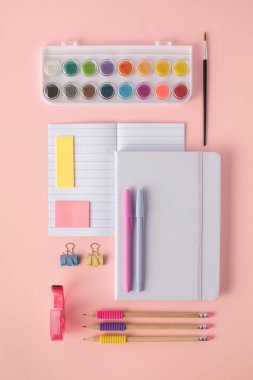 Kırtasiye malzemesi, not defteri ve pembe arka planda boyalar. Okula Dönüş Konsepti.