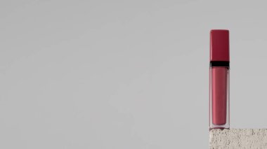 Gri arkaplandaki taş kaidede nemlendirici pembe dudak kremi. Makyaj konsepti, dudak bakımı. Boşluğu kopyala
