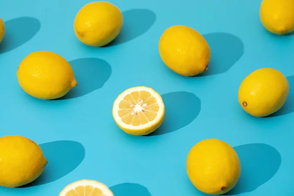 Juicy yellow lemons on a blue background with hard shadows. Summer pattern with ripe lemons. Trendy background.