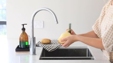 Bir kadın mutfaktaki lavabonun üzerinde sebze soyacağı ile patates soyuyor. Yemek pişirme süreci, sebze kökü..
