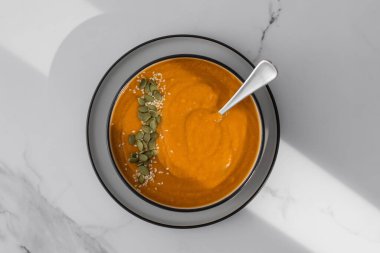 Patates püresi ve çekirdekli bir kase balkabağı çorbası pencerenin gölgesiyle bir ışık masasında duruyor. Sonbahar menüsü konsepti. Kolay vejetaryen tarifleri.