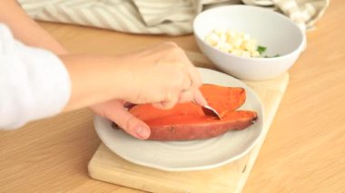 Bir kadın fırında tatlı patatesi ikiye böler. Portakallı kumara, tatlı patates. Kök ekin hasadı. Sağlıklı beslenme kavramı. 