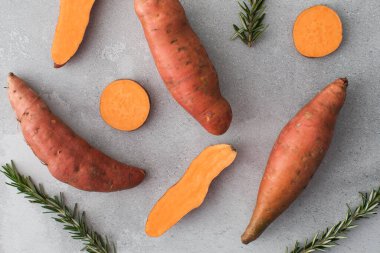Çiğ patatesler bir bütün ve gri bir arka planda kesilmiş. Portakallı kumara, tatlı patates. Kök ekin hasadı. Sağlıklı beslenme kavramı.