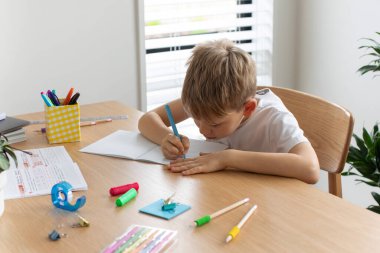 Evde ödev yapan sevimli çocuk. Uzaktan eğitim. Online eğitim. Çocuk dikkatle bir deftere yazıyor..